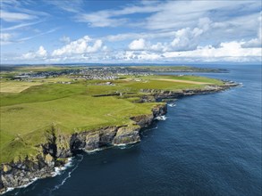 Aerial view of rugged cliffs on the North Sea coast, with the harbour town of Wick on the horizon,