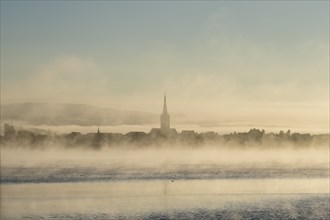 Early morning mist drifts over Lake Constance, on the horizon the silhouette of the old town with