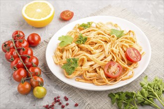 Semolina pasta with tomato pesto sauce, orange and herbs on a white ceramic plate on a gray