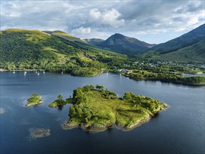 Aerial view of the island of Eilean Munde, behind it the village of Ballachulish with the harbour