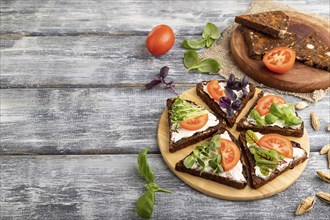 Grain rye bread sandwiches with cream cheese, tomatoes and microgreen on gray wooden background and