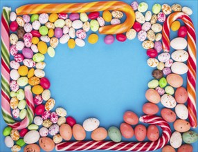 Colorful frame of multicolored candies on a blue background. Christmas cane, chocolate eggs,