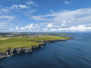 Aerial view of rugged cliffs on the North Sea coast, with the harbour town of Wick on the horizon,