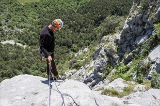 A climber in safety equipment descends a rocky mountain face, alpine climbing with rope, Arco,