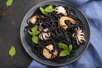 Black cuttlefish ink pasta with shrimps or prawns and small octopuses on black concrete background