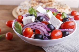 Greek salad with fresh cherry tomatoes, feta cheese, black olives, basil and onion on wooden