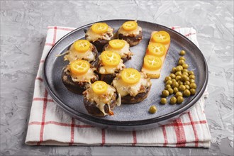 Stuffed fried champignons with cheese, kumquats and green peas on a gray concrete background.