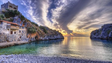 Colourful sunrise on a pebble beach with cliffs and historic building, Mani Peninsula, Peloponnese,