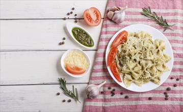 Farfalle pasta with pesto sauce, tomatoes and cheese on a linen tablecloth on white wooden