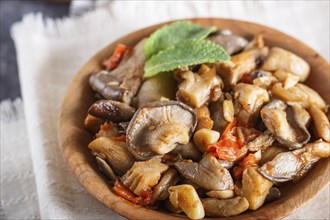 Fried oyster mushrooms with tomatoes in wooden plate on black concrete background. top view, close