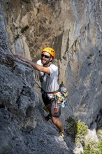 A climber with helmet and safety equipment scales a steep rock face, alpine climbing with rope,