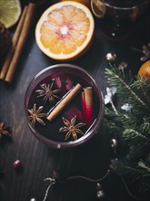 Glass of traditional mulled wine with orange and cranberry garnishes on a cozy Christmas table. The