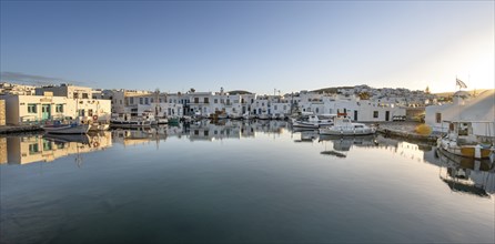 Fishing boats in the harbour of Naoussa at sunset, reflected in the sea, White Cycladic houses,