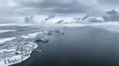 Aerial panorama of the snow-covered Mettnau peninsula with the Mettnau park, spa centre and beach