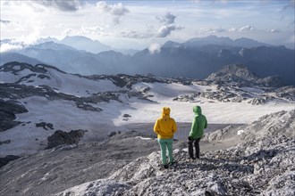 High alpine landscape, snowfields and rock, Two hikers look down into the valley from the