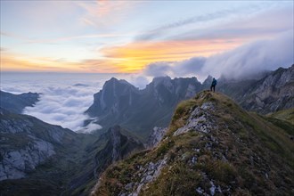 Hiker on the mountain, view over SÃ¤ntis mountains into the valley of Meglisalp at sunrise, high