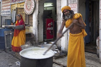 Hindu man wearing red bindi on forehead stirring food in huge pot for the needy in Udaipur,