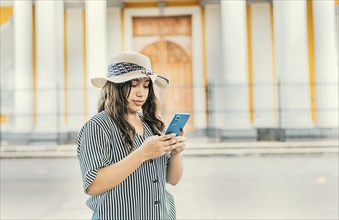 The girl wears a hat, stands in front of a Catholic church with a blurred background, is smiling