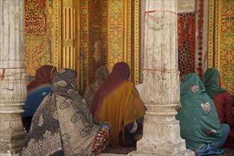 Muslim women wearing colourful headscarfs and saris praying at the Nizam-Ud-Din shrine in Delhi,