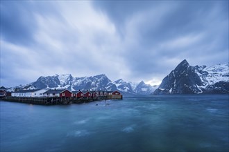 Rorbuer cabins of Hamnoy by the fjord, snowy mountains in the back, Hamnoy, Reine, Moskenesoya,