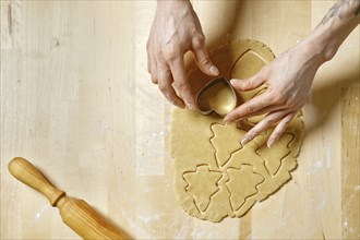 Top view at hands of unrecognizable woman cutting out biscuits from dough with cookie cutter