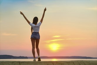 Cute woman meets sunset on a pier, back view