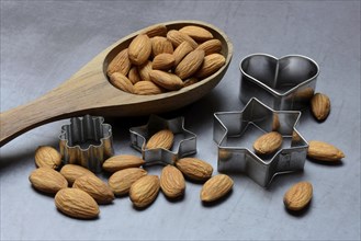 Wooden ladle with almonds and cookie cutters, baking ingredient