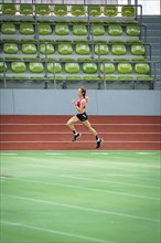 Lone runner trains on the running track of an empty stadium with green rows of seats, Glaspalast,