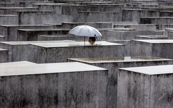 A visitor to the Memorial to the Murdered Jews of Europe protects himself from heavy rain with an