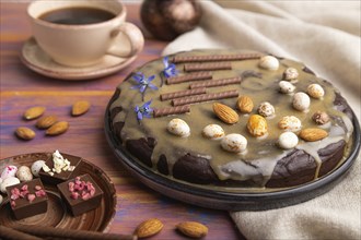 Homemade chocolate brownie cake with caramel cream and almonds with cup of coffee on a colored