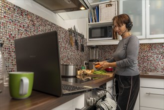 Woman, mid-50s, works from home, with laptop and communicates with colleagues via headset, home