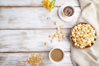 Popcorn with caramel in wooden bowl and a cup of coffee on a white wooden background and linen