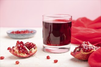 Glass of pomegranate juice on a white and pink background with red textile. Side view, close up,