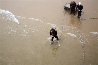 Looking down from above at professional divers on a beach about to enter the sea to work on the