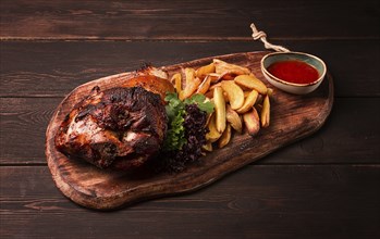 Pork knuckle, in soy-honey sauce, with fried potatoes, on a wooden chopping board, homemade, no