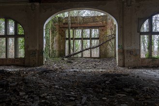 Interior view of a dilapidated building with arched windows and debris on the floor,