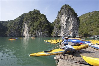 Vietnamese men pull a kayak onto a jetty, behind them the karst rocks of Lan Ha Bay, Halong Bay,