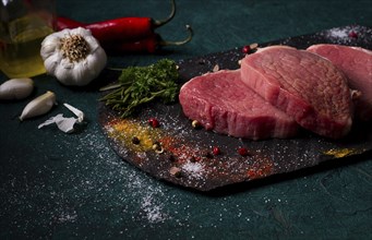 Fresh raw beef meat, Medallions, on black slate, with spices, close-up, horizontal