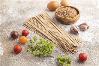 Japanese buckwheat soba noodles with tomato, eggs, spices, herbs on brown concrete background. Side