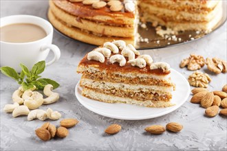 Piece of homemade cake with caramel cream and nuts with cup of coffee on a gray concrete background