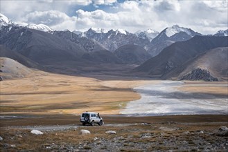 Off-road vehicle on a gravel track, glaciated and snow-covered peaks, Ak Shyrak Mountains, near