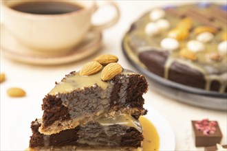 Pieces of chocolate brownie cake with caramel cream and almonds on a white concrete background.