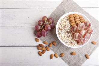 A plate with muesli, almonds, pink grapes on a white wooden background. top view. copy space