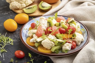 Vegetarian salad of cauliflower cabbage, kiwi, tomatoes, microgreen sprouts on black concrete