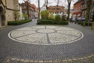 Rosette of white cobblestones at St Laurentius Church with historic houses and trees in the