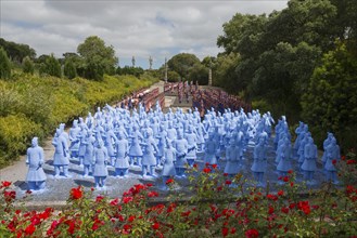 Numerous blue terracotta soldier statues stand on a path lined with flowers and trees, Bacalhôa,