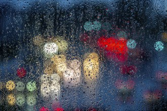 Rainy weather, road traffic, raindrops on a window pane, behind, blurred, lights of vehicles on a