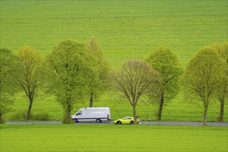 Car on a country road, overtaking manoeuvre, green fields, meadows, trees line the 2-lane road,