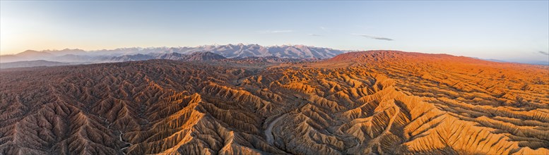 Panorama, riverbed runs through a landscape of eroded hills, badlands at sunrise, mountain peaks of