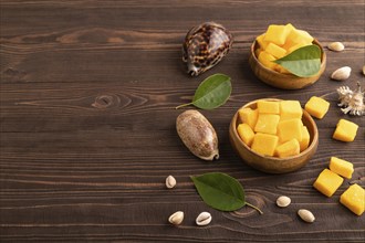 Dried and candied mango cubes in wooden bowls on brown wooden textured background. Side view, copy